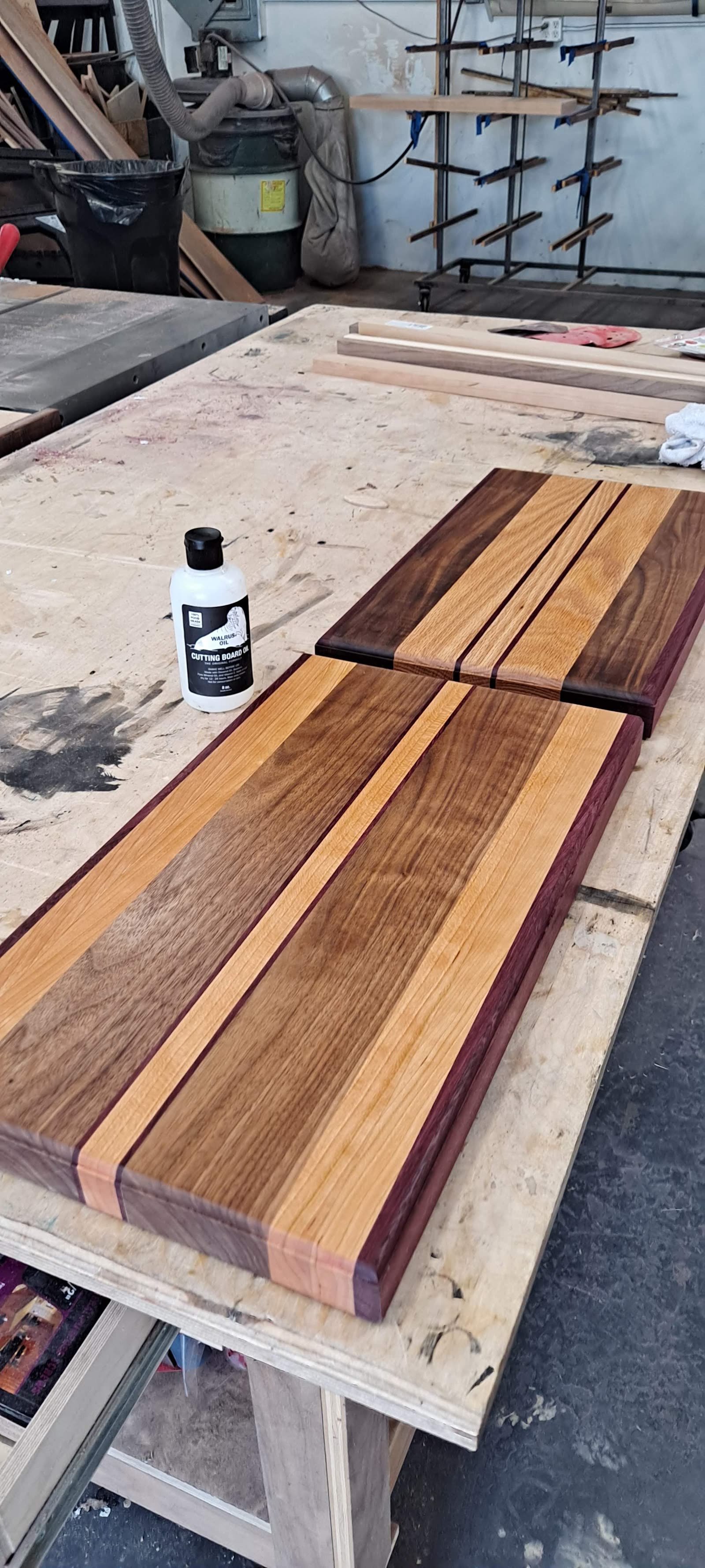 A pair of striped edge-grain boards in mixed hardwoods on the bench, next to a bottle of finishing oil