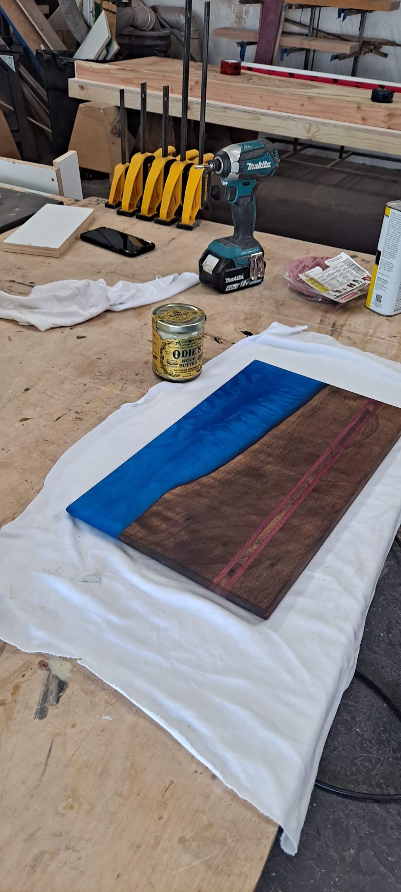 Dark walnut piece with a wide blue epoxy river and a thin red line, laid out on a cloth in the shop