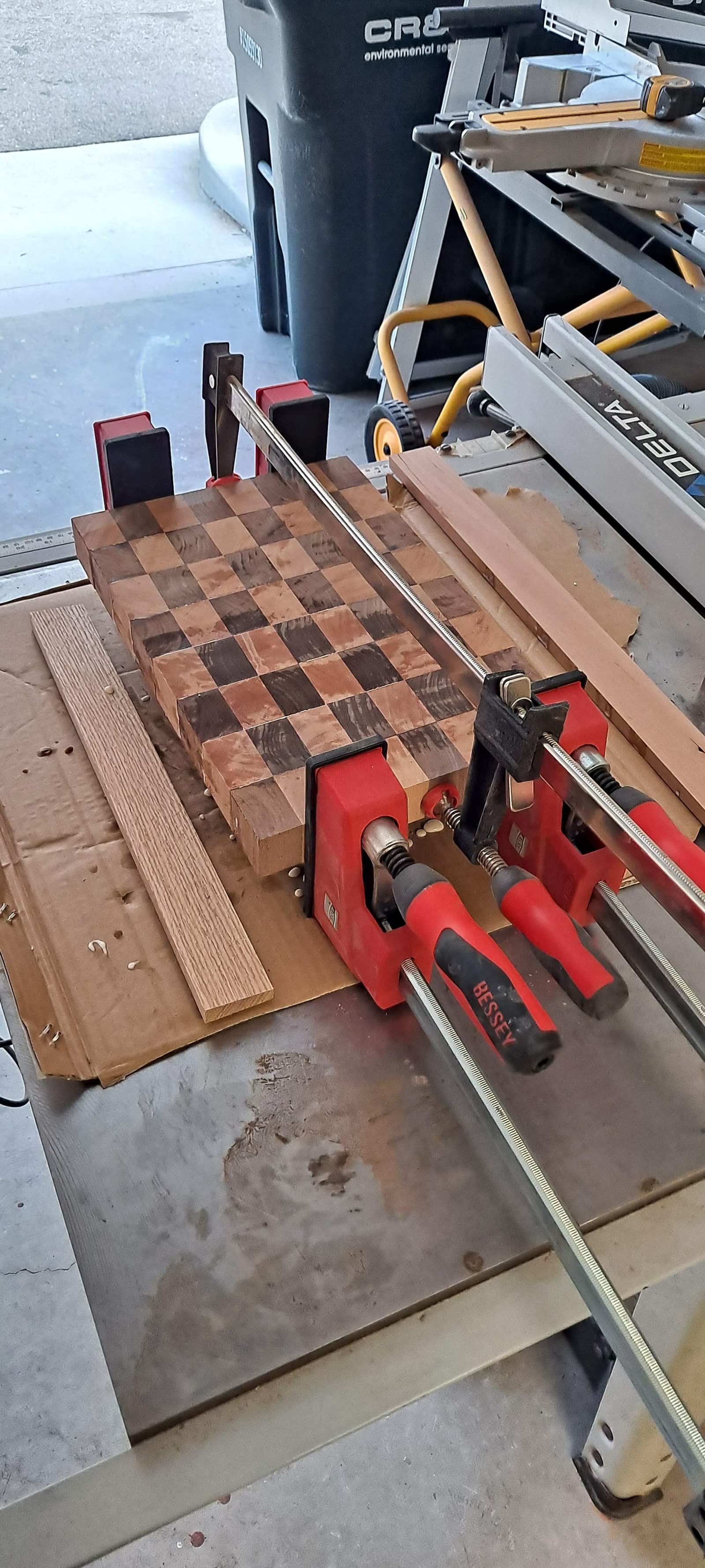 Checkerboard-pattern end-grain cutting board clamped up during glue-up on the workbench